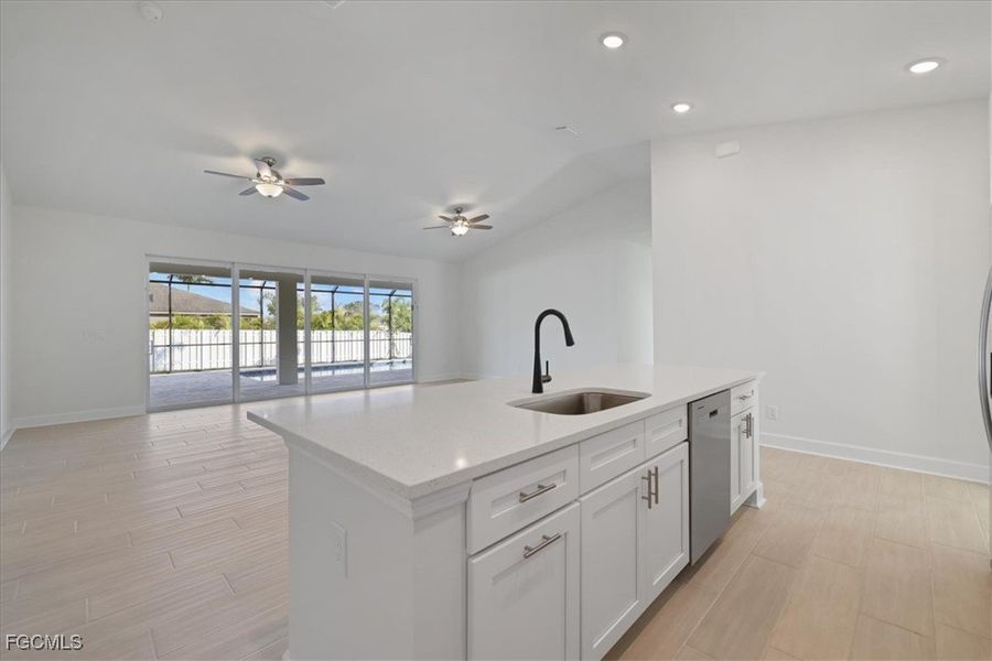 Kitchen featuring lofted ceiling, wood finish floors, a center island with sink, light stone counters, and open floor plan Kitchen featuring lofted ceiling, wood finish floors, a center island with sink, light stone counters, and open floor plan