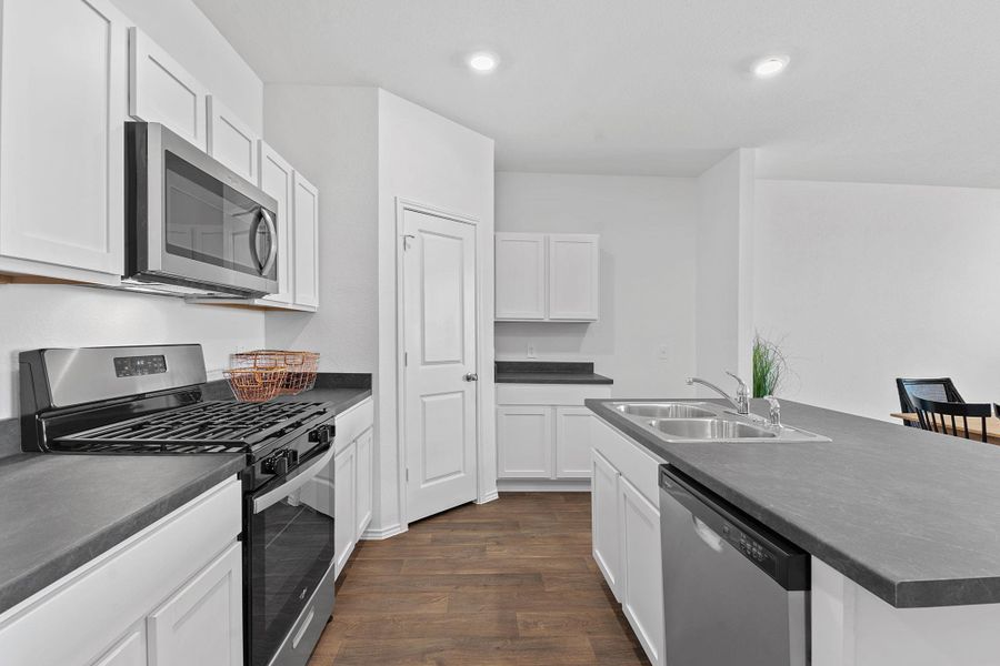 Kitchen featuring dark wood finished floors, dark countertops, stainless steel appliances, white cabinetry, and a sink