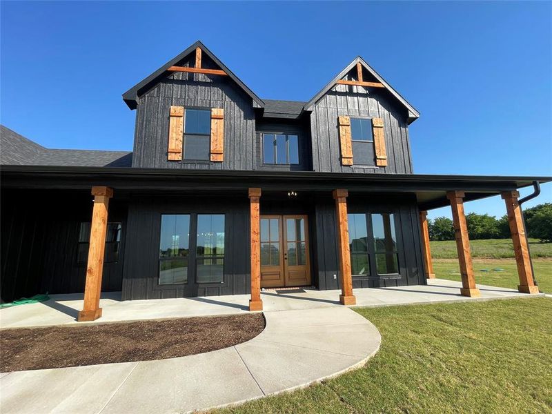 Modern farmhouse exterior featuring black vertical siding, a covered porch with exposed wood beams, and a concrete pathway