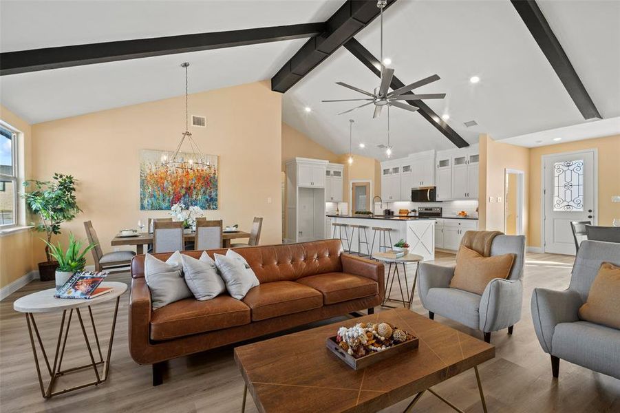 Open-concept living space featuring vaulted ceilings with exposed beams, wood-finish flooring, a contemporary ceiling fan, recessed lighting, and a modern kitchen with an island and integrated appliances Open-concept living space featuring vaulted ceilings with exposed beams, wood-finish flooring, a contemporary ceiling fan, recessed lighting, and a modern kitchen with an island and integrated appliances