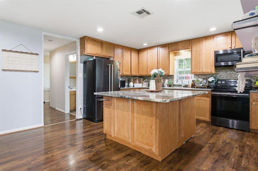 Kitchen featuring a central island with a stone countertop, wood cabinetry, wood-finish flooring, a stainless steel oven with an overhead microwave, and a black refrigerator