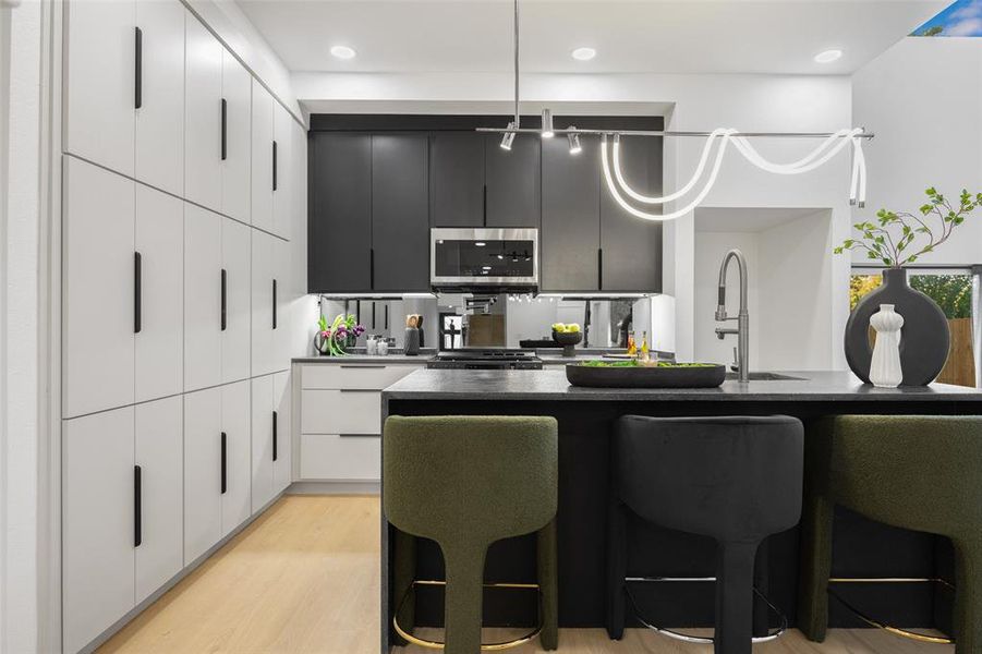 Kitchen with a kitchen breakfast bar, modern cabinets, dark cabinets, pendant lighting, and stainless steel microwave