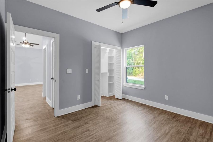 Unfurnished bedroom featuring a walk in closet, wood finished floors, and ceiling fan
