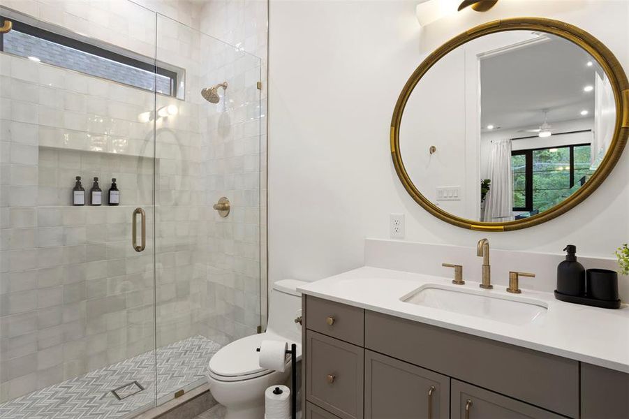 Well-appointed bathroom featuring a glass-enclosed shower with chevron-patterned floor tile, a single vanity with a white countertop, and a circular mirror with an ornate frame