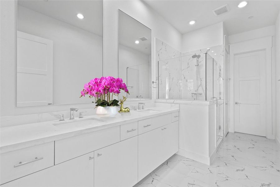 Bathroom featuring a marble finish shower, double vanity, light marble finish floors, and recessed lighting