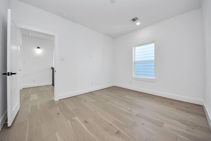 This room offers a minimalist design with light wood floors, white walls, and recessed lighting. A single window lets in natural light, while a white door connects to a well-lit hallway, offering versatility for a bedroom, office, or other use. This room offers a minimalist design with light wood floors, white walls, and recessed lighting. A single window lets in natural light, while a white door connects to a well-lit hallway, offering versatility for a bedroom, office, or other use.