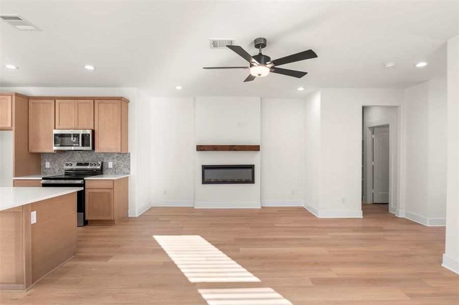 Kitchen featuring tasteful backsplash, stainless steel appliances, open floor plan, recessed lighting, and a glass covered fireplace