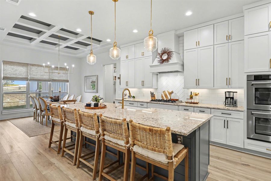 Kitchen with coffered ceiling, light stone countertops, pendant lighting, stainless steel appliances, and a breakfast bar area