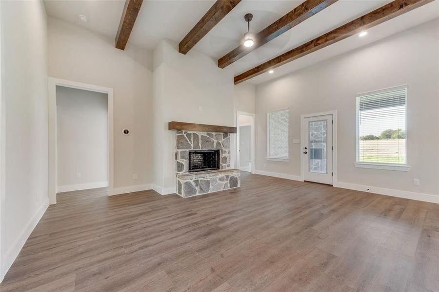 Unfurnished living room with beam ceiling, ceiling fan, a fireplace, and light hardwood / wood-style floors