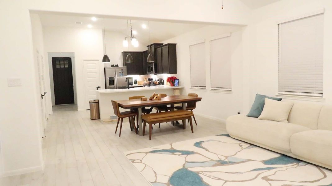 This open-concept living space features a modern kitchen with dark cabinets, stainless steel appliances, and pendant lighting. Adjacent is a dining area and the living area includes a comfortable sofa and a stylish rug, creating a cozy and inviting atmosphere. This open-concept living space features a modern kitchen with dark cabinets, stainless steel appliances, and pendant lighting. Adjacent is a dining area and the living area includes a comfortable sofa and a stylish rug, creating a cozy and inviting atmosphere.