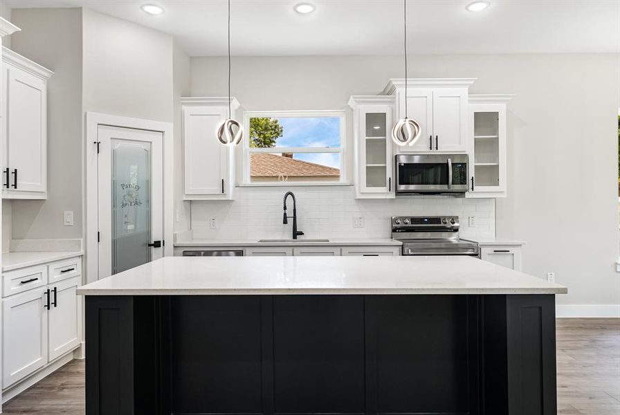 Kitchen featuring appliances with stainless steel finishes, wood finished floors, decorative backsplash, glass insert cabinets, and recessed lighting Kitchen featuring appliances with stainless steel finishes, wood finished floors, decorative backsplash, glass insert cabinets, and recessed lighting