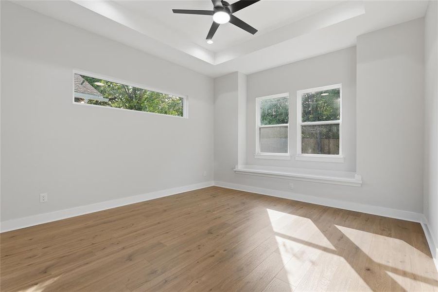 Spacious room featuring wood-finish flooring, a contemporary ceiling fan, and a tray ceiling Spacious room featuring wood-finish flooring, a contemporary ceiling fan, and a tray ceiling
