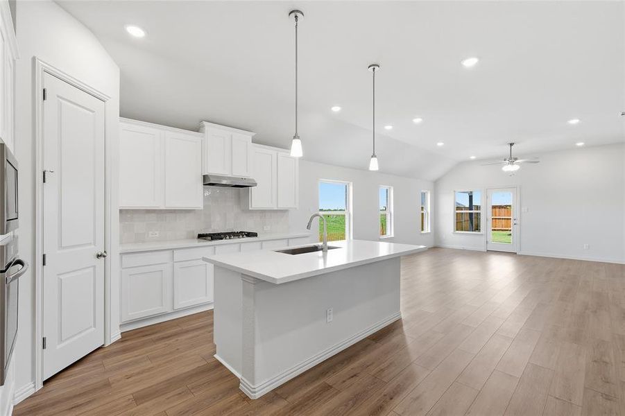 Kitchen with backsplash, white cabinets, an island with sink, lofted ceiling, and dark wood-style floors