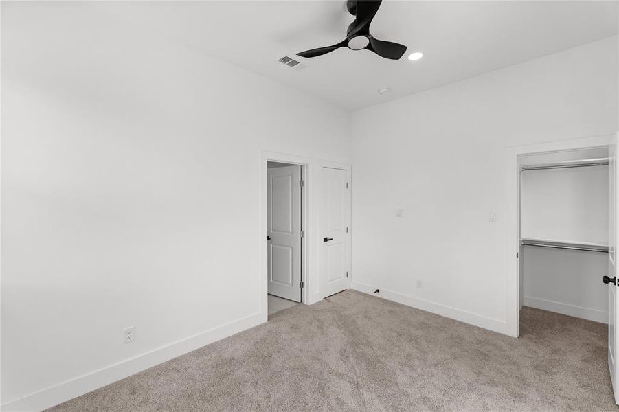 Carpeted room with white walls, a contemporary black ceiling fan with integrated lighting, and a closet with built-in shelving