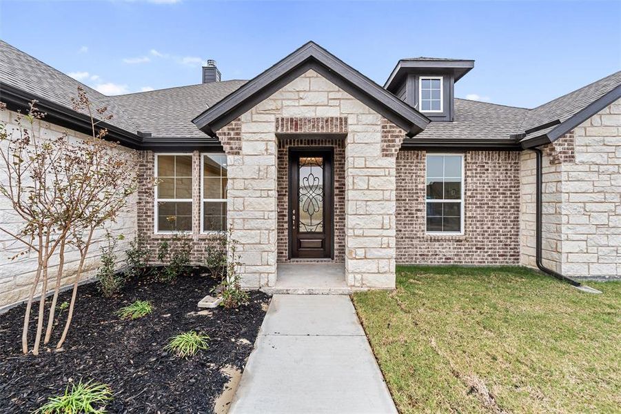 Doorway to property featuring roof with shingles, brick siding, a yard, a chimney, and stone siding