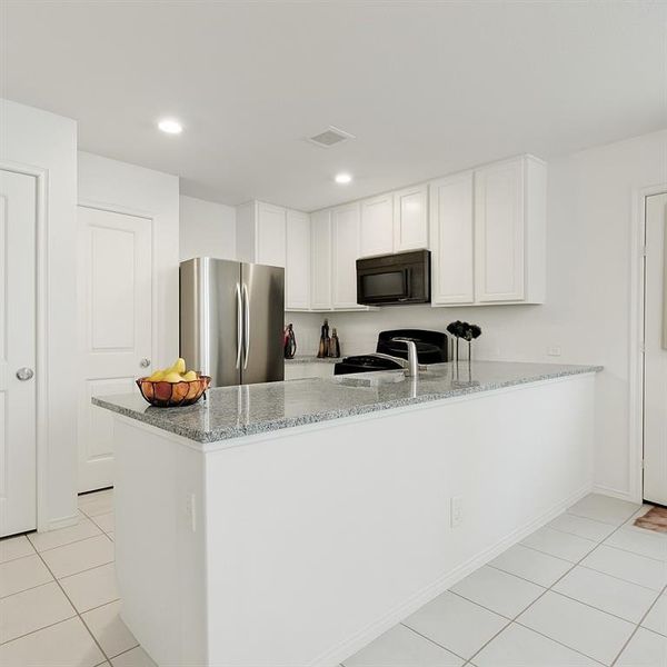 Kitchen featuring light stone countertops, freestanding refrigerator, light tile patterned floors, black microwave, and white cabinets Kitchen featuring light stone countertops, freestanding refrigerator, light tile patterned floors, black microwave, and white cabinets