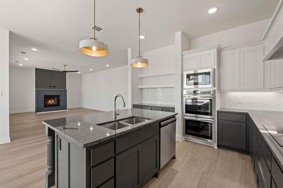 Kitchen with a sink, appliances with stainless steel finishes, a brick fireplace, dark stone counters, and open shelves