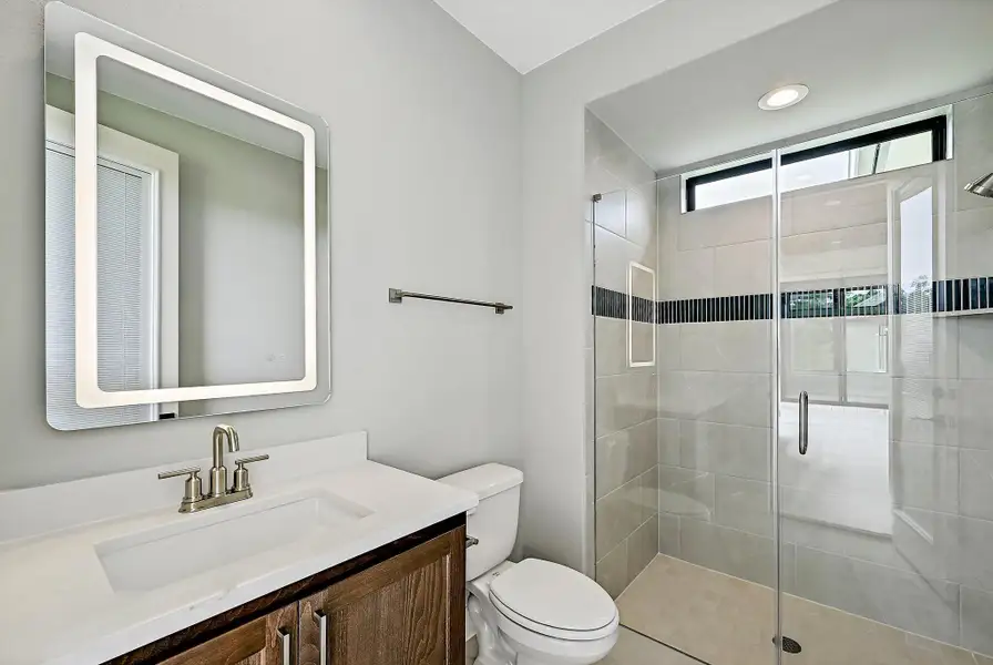 Modern bathroom featuring a vanity with a sleek countertop, an illuminated mirror, and a tiled walk-in shower.