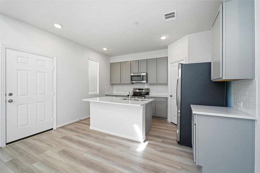 Kitchen with gray cabinetry, stainless steel appliances, a center island with sink, decorative backsplash, and recessed lighting