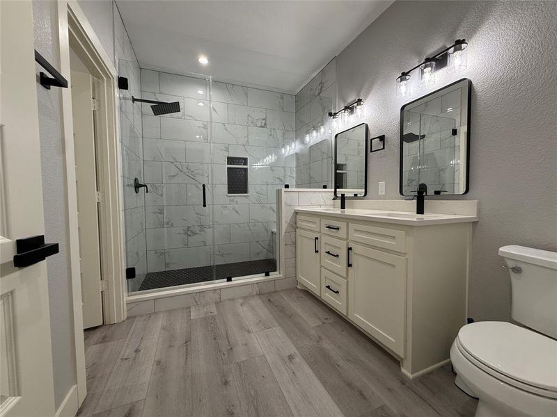 Full bathroom featuring light wood-style flooring, double vanity, a textured wall, and a stall shower