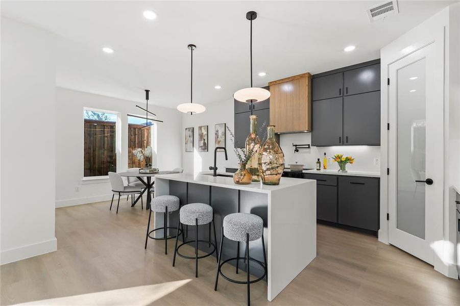 Kitchen with a breakfast bar area, decorative light fixtures, a center island with sink, light wood-style flooring, and gray cabinets