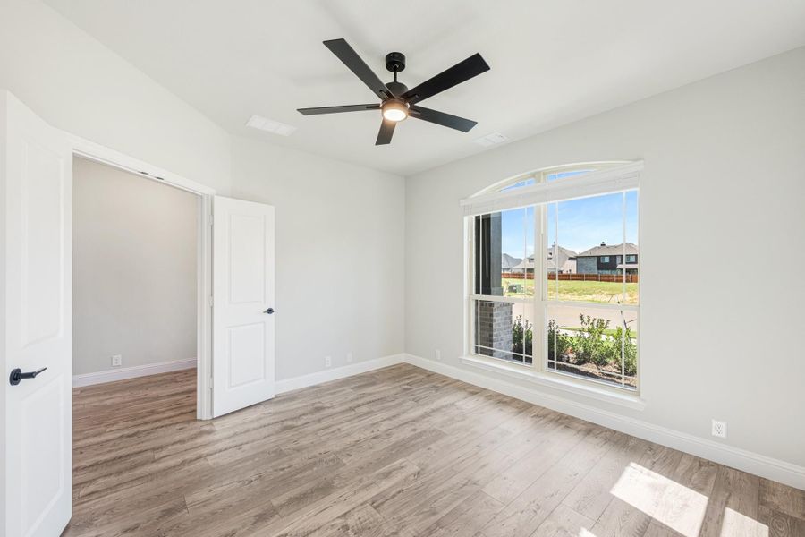 Empty bedroom with wood-look floors, black ceiling fan, and arched window with neighborhood view