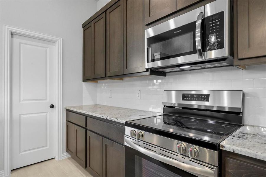 Kitchen featuring dark brown cabinetry, appliances with stainless steel finishes, light stone countertops, and tasteful backsplash