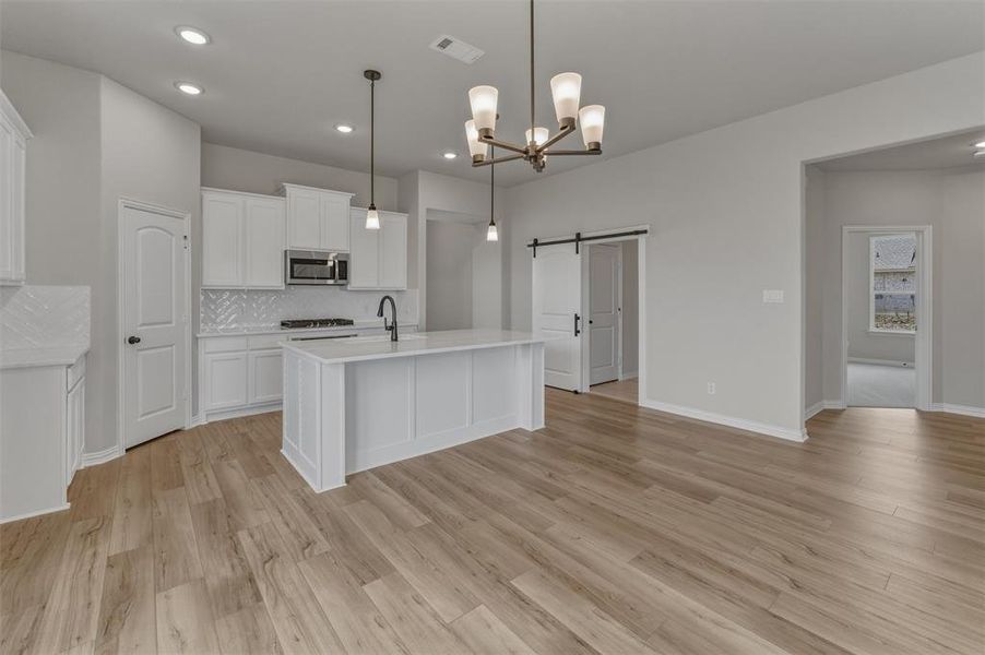 Open-concept kitchen featuring white cabinetry, a central island, stainless steel appliances, a tile backsplash, and wood-finish flooring Open-concept kitchen featuring white cabinetry, a central island, stainless steel appliances, a tile backsplash, and wood-finish flooring