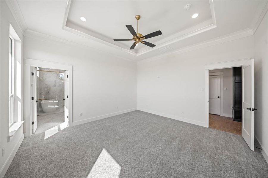 Unfurnished bedroom with light colored carpet, a ceiling fan, crown molding, and ensuite bathroom