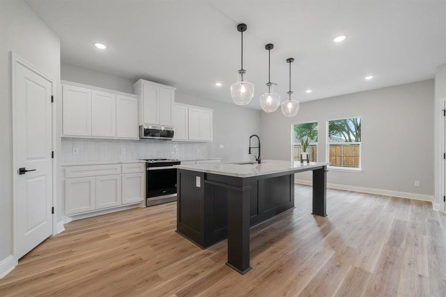 Kitchen with a center island with sink, tasteful backsplash, light wood-type flooring, appliances with stainless steel finishes, and pendant lighting