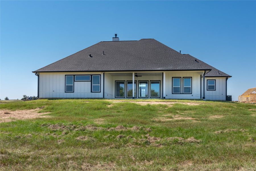This photo showcases the back view of a modern single-story house with a large, sloped roof and a spacious patio area. The exterior features a crisp, white finish with contrasting dark window frames and a well-maintained lawn, providing an open landscape. This photo showcases the back view of a modern single-story house with a large, sloped roof and a spacious patio area. The exterior features a crisp, white finish with contrasting dark window frames and a well-maintained lawn, providing an open landscape.