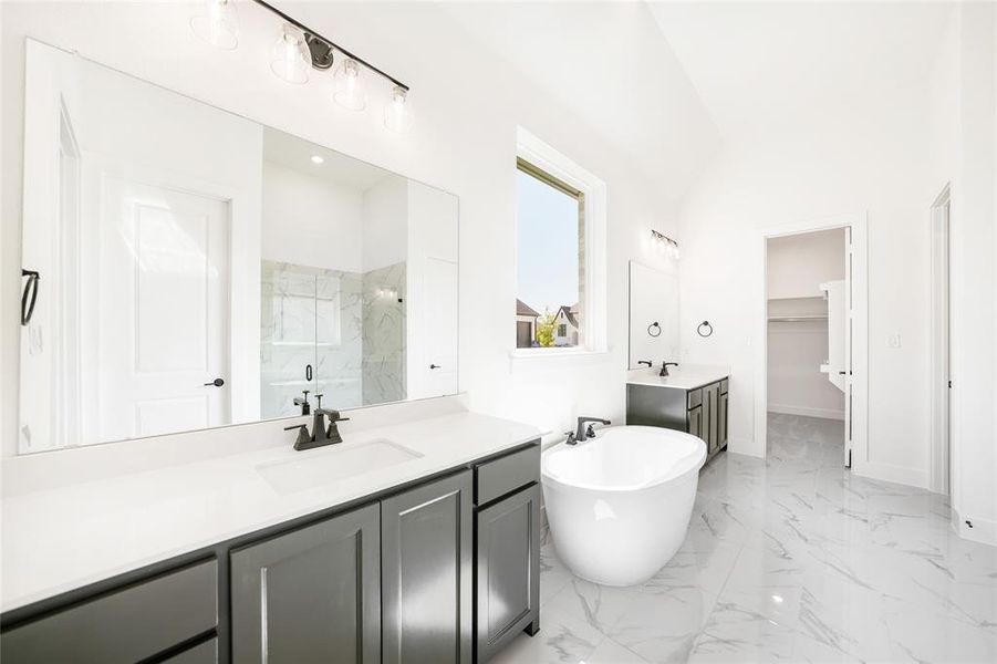 Bathroom featuring a marble finish shower, a freestanding tub, two vanities, light marble finish floors, and a spacious closet