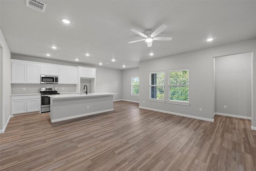 Kitchen with white cabinetry, appliances with stainless steel finishes, light wood-style floors, a kitchen island with sink, and recessed lighting Kitchen with white cabinetry, appliances with stainless steel finishes, light wood-style floors, a kitchen island with sink, and recessed lighting
