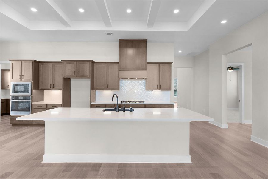 Kitchen with recessed lighting, stainless steel appliances, a kitchen island with sink, light stone counters, and beamed ceiling