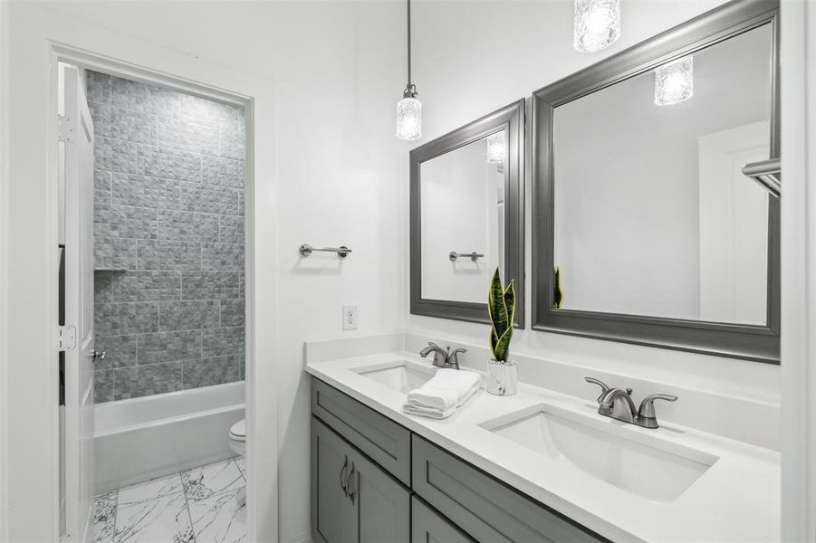 Full bathroom with double sink vanity, toilet, tiled shower / bath combo, and tile patterned flooring