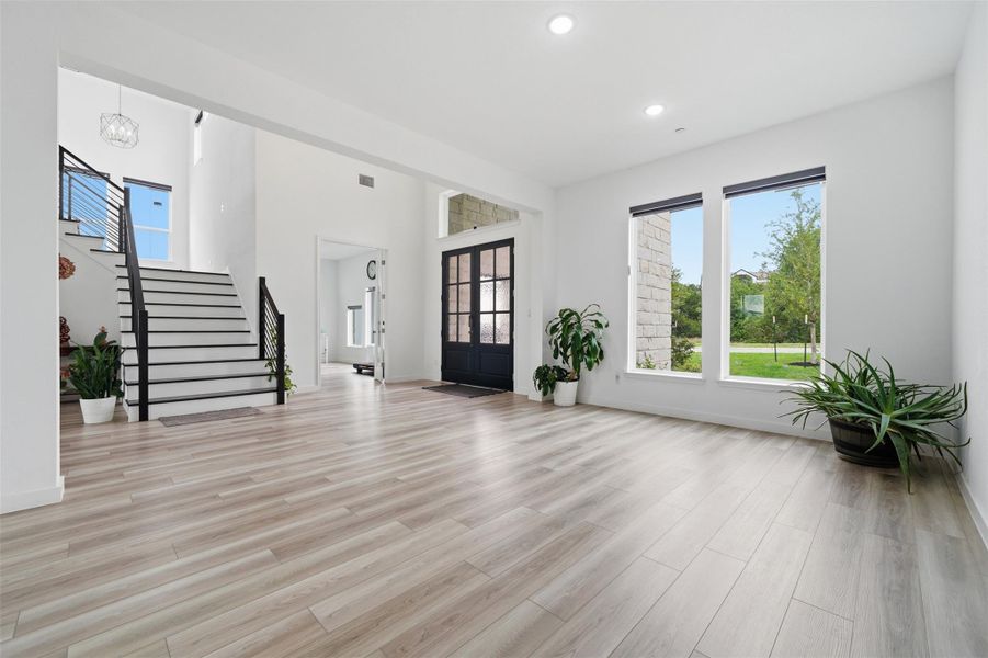 Spacious entryway featuring light-toned flooring, a grand staircase with black railings, and large windows that provide views of the outdoors