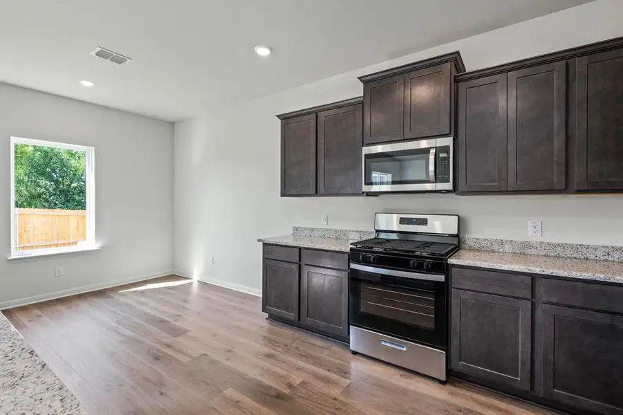 Kitchen with stainless steel appliances, dark brown cabinets, light stone counters, light wood-type flooring, and recessed lighting Kitchen with stainless steel appliances, dark brown cabinets, light stone counters, light wood-type flooring, and recessed lighting