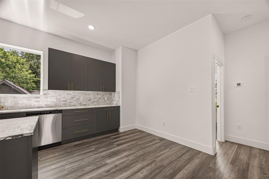 This modern kitchen features sleek dark cabinetry, stainless steel appliances, and a stylish tile backsplash. The space is bright with natural light from a large window, complemented by elegant wood flooring. This modern kitchen features sleek dark cabinetry, stainless steel appliances, and a stylish tile backsplash. The space is bright with natural light from a large window, complemented by elegant wood flooring.