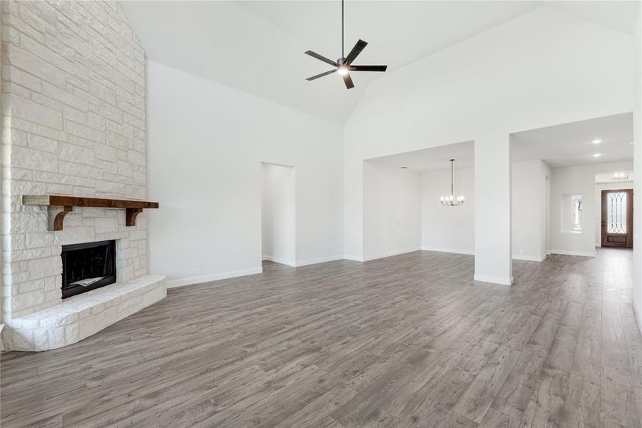 Open living room with stone fireplace, vaulted ceiling, ceiling fan, and gray hardwood floors leading to dining area