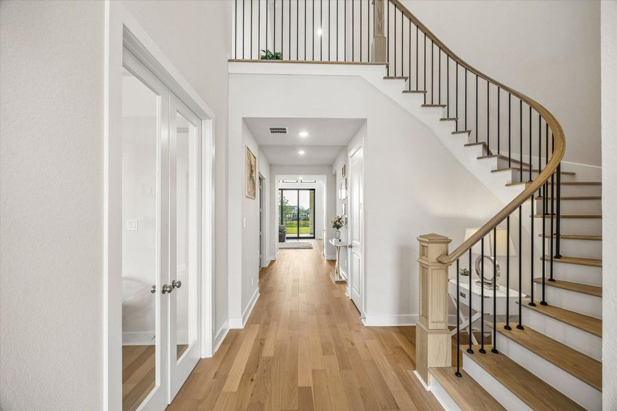 BRIGHT ENTRY HALL FEATURES WIDE-PLANK WOOD FLOORING AND A CURVED STAIRCASE WITH WOOD TREADS AND BLACK IRON BALUSTERS. BRIGHT ENTRY HALL FEATURES WIDE-PLANK WOOD FLOORING AND A CURVED STAIRCASE WITH WOOD TREADS AND BLACK IRON BALUSTERS.