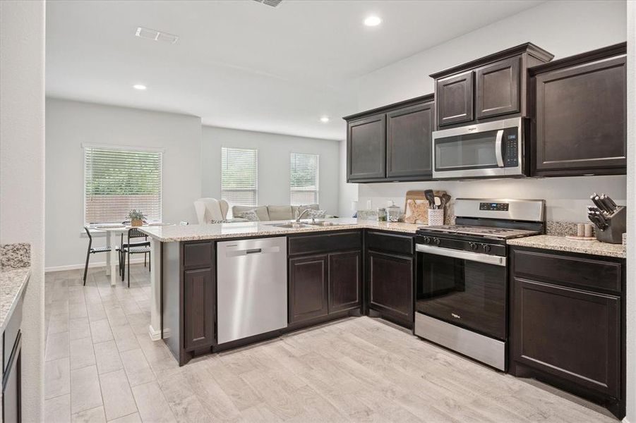 Kitchen featuring dark brown cabinets, appliances with stainless steel finishes, recessed lighting, light wood-style floors, and light stone countertops. Kitchen featuring dark brown cabinets, appliances with stainless steel finishes, recessed lighting, light wood-style floors, and light stone countertops.