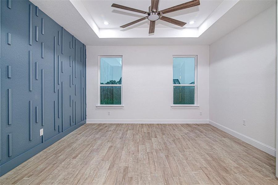 Empty room with a raised ceiling, a ceiling fan, light wood-type flooring, recessed lighting, and baseboards Empty room with a raised ceiling, a ceiling fan, light wood-type flooring, recessed lighting, and baseboards