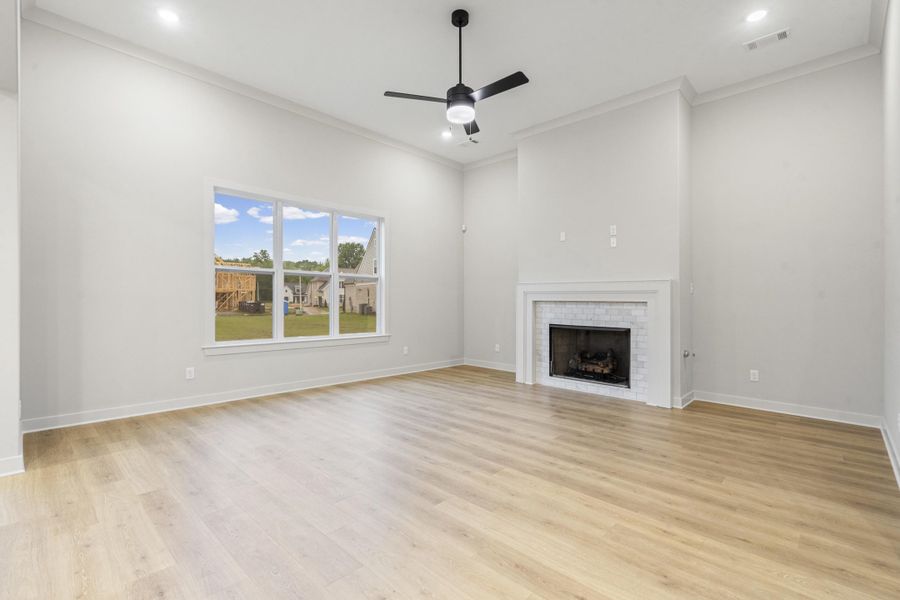 Spacious living area featuring high ceilings, wood-finish flooring, a white brick-surround fireplace with mantel, recessed lighting, and a modern ceiling fan Spacious living area featuring high ceilings, wood-finish flooring, a white brick-surround fireplace with mantel, recessed lighting, and a modern ceiling fan