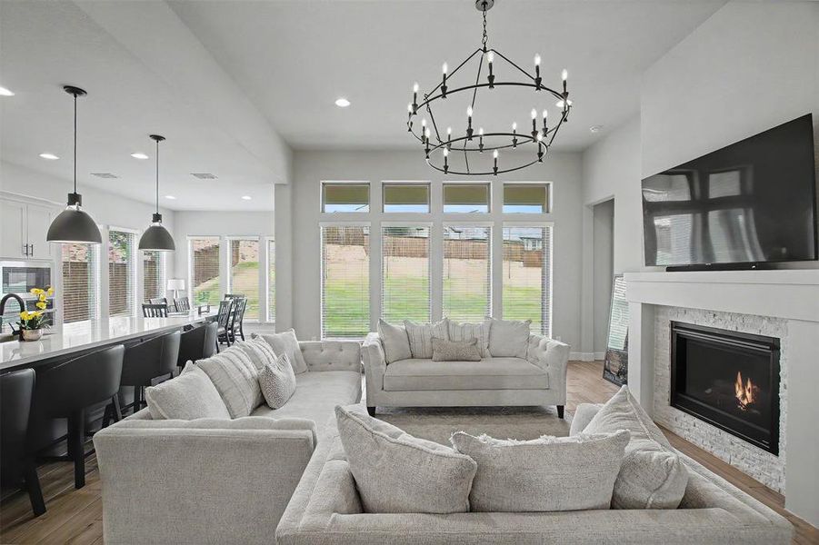Open-concept living space featuring a contemporary fireplace with a stone surround, a prominent chandelier, recessed lighting, and expansive windows