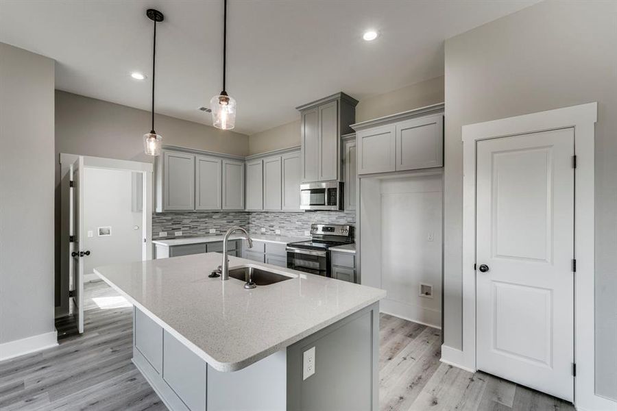 Kitchen featuring stainless steel appliances, a kitchen island with sink, sink, tasteful backsplash, and light hardwood / wood-style floors