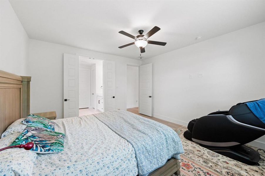 Bedroom featuring light wood-finish flooring, a ceiling fan with integrated lighting, and white walls Bedroom featuring light wood-finish flooring, a ceiling fan with integrated lighting, and white walls