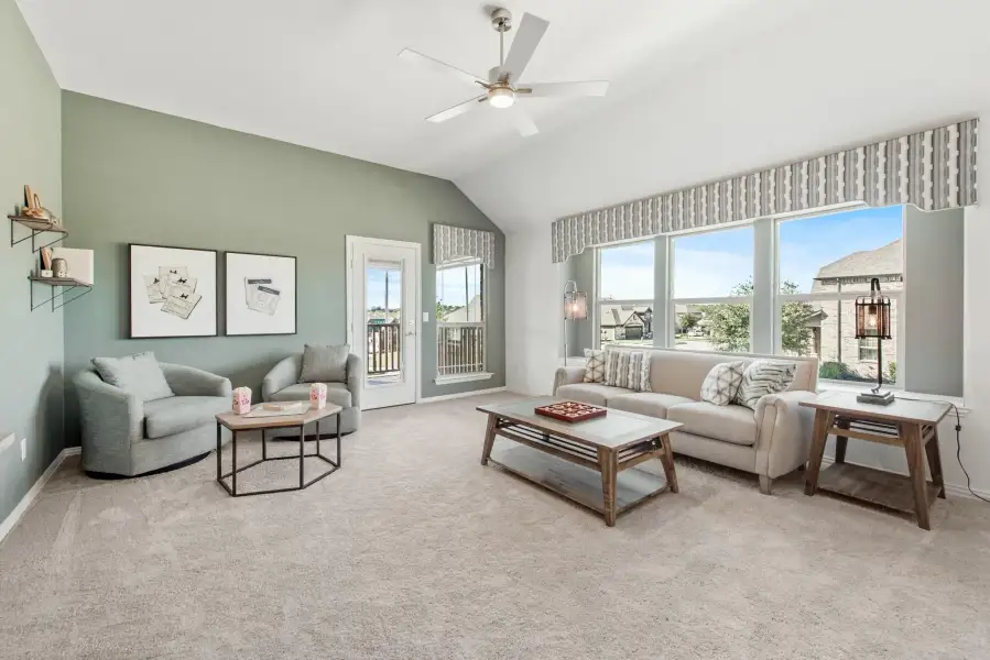 Living room with vaulted ceiling, ceiling fan, large windows, and neutral carpet with sage green accent wall