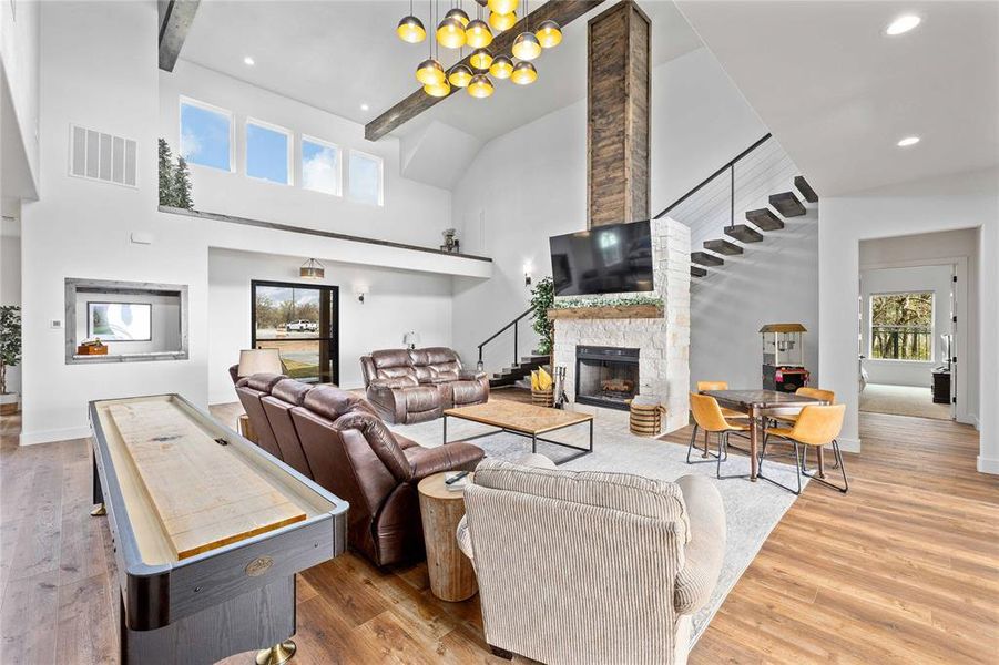 Living area featuring a stone fireplace, light wood-style floors, high vaulted ceiling, recessed lighting, and a chandelier