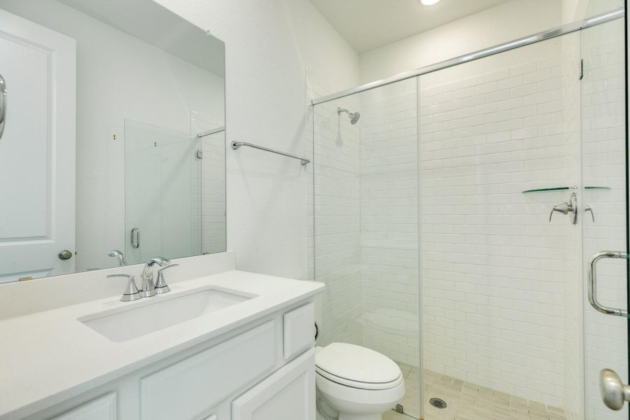 Guest bathroom featuring a sleek glass walk-in shower, elegant quartz countertops, and durable, stylish tile flooring.