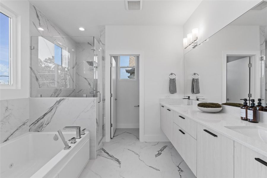 Spa-like primary bath featuring a floating double vanity, soaking tub & frameless glass shower all wrapped in elegant marble-inspired tile for a clean, modern finish. Spa-like primary bath featuring a floating double vanity, soaking tub & frameless glass shower all wrapped in elegant marble-inspired tile for a clean, modern finish.